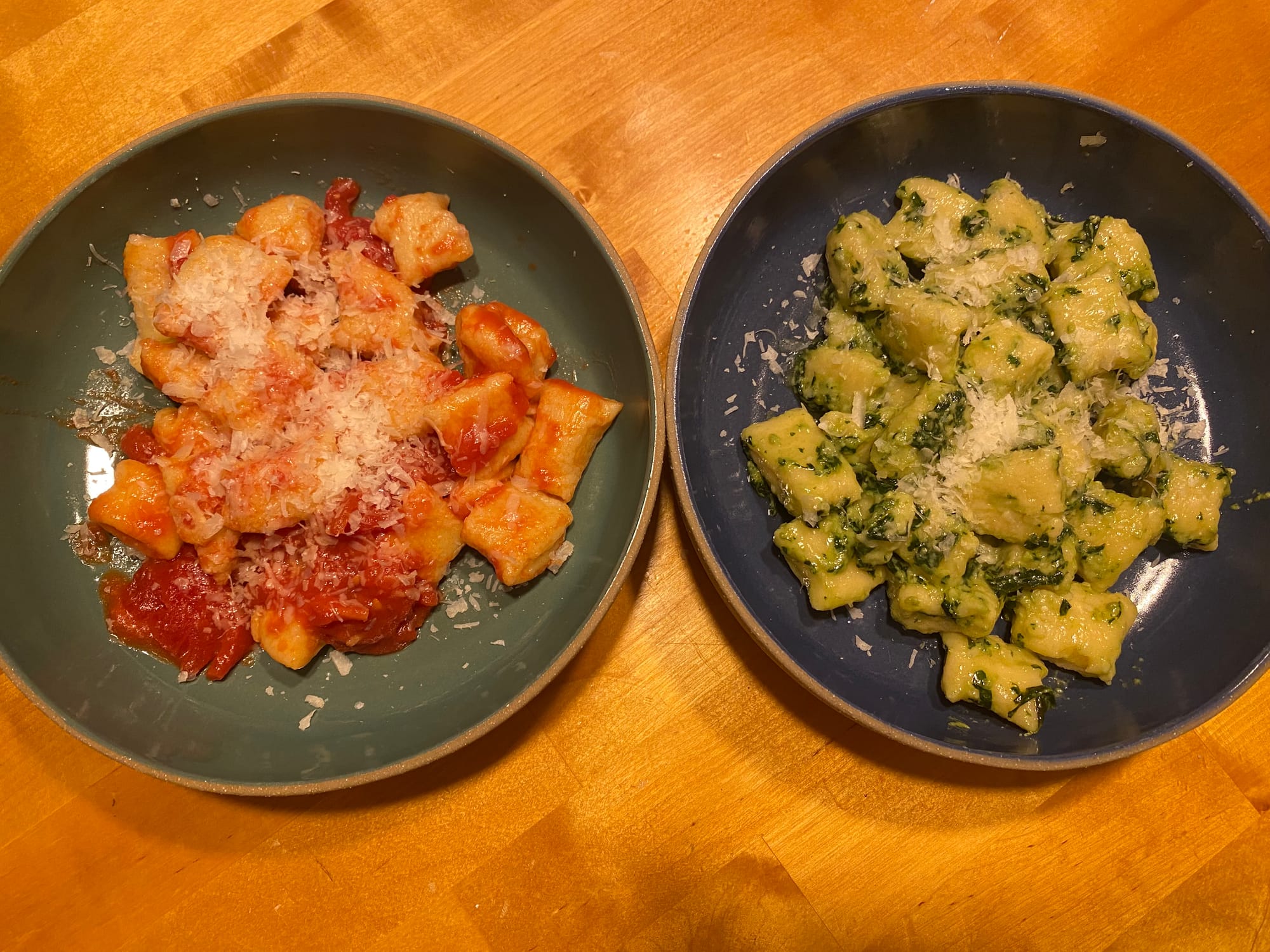 A mediocre photo of two dishes of very delicious homemade gnochhi, one with a red sauce and one with a pesto