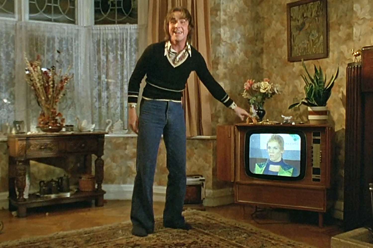 A still from Velvet Goldmine showing a teenage Christian Bale excitedly yelling "that's me!" and pointing at the TV, on which Jonathan Rhys Meyer's character is coming out as bisexual