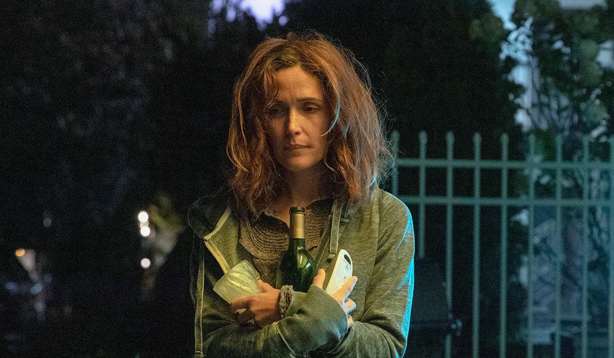 A still from If I Had Legs I'd Kick You, showing Rose Byrne clutching a bottle of wine to her chest, looking extremely frazzled and exhausted, her hair a damn rat's nest